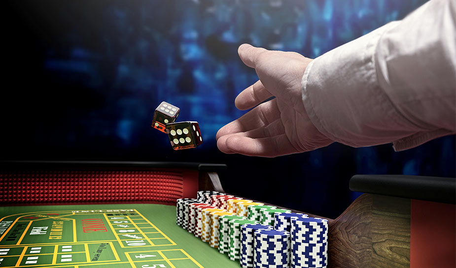 man gooit twee dobbelstenen op een groene crapstafel met casino fiches